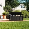 A garden bench with storage, filled with cushions, is placed on a wooden deck in a backyard setting with lush green grass and trees. Produktbild-Vorschau