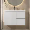 A white wall-mounted bathroom vanity with two drawers and a cabinet door, set against a wood-paneled wall with a large illuminated mirror above. Náhled obrázku produktu