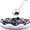 A close-up shot of a sieve filled with black tapioca pearls, hovering over a bowl of the same pearls. Produktbild-Vorschau