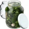 Two glass jars, one empty and one filled with pickles, dill, and garlic, with a white lid next to it. Podgląd zdjęcia produktu