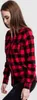A woman wearing a red and black checkered flannel shirt and black jeans, posing against a white background. Náhled obrázku produktu