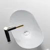 A top-down view of a white oval vessel sink with a black and gold faucet. Náhľad obrázku produktu
