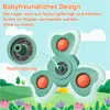 A close-up of a green and white fidget spinner toy with orange balls, set against a cartoonish background of a green landscape with flowers and trees. Produktbild-Vorschau
