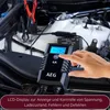 A hand is shown pressing a button on a car battery charger connected to a car battery under the hood. Produktbild-Vorschau