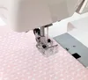 A close-up view of a sewing machine needle and presser foot sewing pink fabric with a leaf pattern. Produktbild-Vorschau