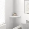 A white corner shelf with decorative items on it, next to a window with blinds. Voir les images du produit