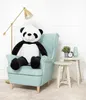 A large plush panda sits in a light blue armchair next to a floor lamp and small side tables. Podgląd zdjęcia produktu