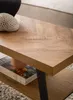 A close-up view of a wooden coffee table with a herringbone pattern, showing a book and a decorative coral on its surface. The table has a shelf underneath. Voir les images du produit
