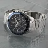 A close-up, angled shot of a men's wristwatch on a reflective gray surface. Náhľad obrázku produktu