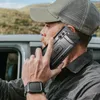 A man wearing a baseball cap is talking on a smartphone while sitting in a vehicle. Produktbild-Vorschau