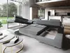 A modern sectional sofa is displayed in an open-concept living room with a large window overlooking a garden. The sofa is partially extended, revealing its storage and bed features. Podgląd zdjęcia produktu