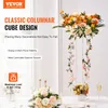 A clear acrylic columnar cube stand decorated with flowers and greenery, set on a table with other floral arrangements and candlesticks. Voir les images du produit