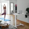 A young girl practices yoga on a mat in a bright, modern living room, while a laptop sits on a mobile standing desk nearby. Voir les images du produit