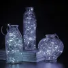 Three glass bottles of varying shapes and sizes, each filled with white LED string lights, are arranged on a surface, possibly books, against a dark background. Voir les images du produit