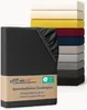 A stack of folded fitted sheets in various colors, with a dark gray fitted sheet in the foreground with a product label. Produktbild-Vorschau