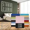 A stack of colorful fitted sheets is displayed in front of a bedroom scene, with icons and text indicating product features. Produktbild-Vorschau