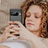 A young woman with curly hair is lying down and looking at her phone, which is in a protective case. Produktbild-Vorschau