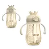 Two views of a baby bottle with a crown-shaped lid and handles, presented on a white background. Produktbild-Vorschau