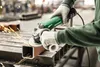 A person is using an angle grinder to cut a metal pipe in a workshop. Anteprima dell’immagine prodotto