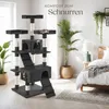 A multi-level cat tree with scratching posts and platforms is set up in a bedroom next to a bed and plants. Náhled obrázku produktu