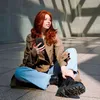 A young woman with red hair sits on the ground, holding a smartphone, in an outdoor urban setting with geometric shadows. Náhľad obrázku produktu