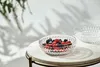 A crystal bowl filled with berries sits on a marble table, with shadows of leaves cast on the wall behind it. Produktbild-Vorschau