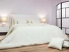 A neatly made bed with white bedding in a room with a light purple wall. Podgląd zdjęcia produktu