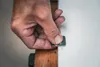 A hand is holding a small metal tool against a white surface, next to a wooden object. Produktbild-Vorschau