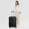 A woman stands next to a black suitcase. Produktbild-Vorschau