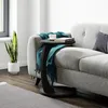 A black C-shaped side table with a book and cup on it, placed next to a grey sofa. A snake plant in a white pot is also visible. Voir les images du produit
