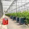 A red electric heater is placed on the floor of a greenhouse, next to rows of plants in containers on carts. Voir les images du produit
