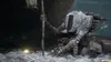 A robotic creature with fur and mechanical parts kneels on the ground, holding a staff with a lantern on top. Produktbild-Vorschau