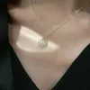Goldene Halskette mit Kleeblatt-Anhänger und klaren Steinen, getragen am Hals einer Person über dunkler Kleidung Náhľad obrázku produktu