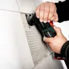 A person is using a Metabo multitool to remove grout from between tiles on a wall. Náhľad obrázku produktu