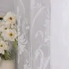 A close-up view of a white sheer curtain with a floral pattern, next to a vase of white flowers. Produktbild-Vorschau