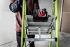 A person wearing work gloves is holding a green Little Giant ladder. Podgląd zdjęcia produktu
