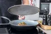 A person is cooking a steak in a pan with a splatter screen over it. Produktbild-Vorschau