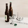 Two beer bottles and two chrome bottle openers shaped like figures on a white surface with a marble-like patterned slab behind them. Náhľad obrázku produktu