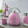 A pink electric kettle and matching mug are displayed on a kitchen countertop with a white subway tile backsplash and a mug tree in the background. Produktbild-Vorschau