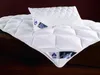 A white quilted duvet and pillow are laid out on a dark wooden surface. Produktbild-Vorschau
