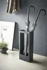 An umbrella stand with two umbrellas inside, placed next to a framed picture and a plant. Produktbild-Vorschau