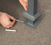 A person is shown installing a metal post into the ground using a screw and anchor. Náhled obrázku produktu