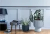 A stylish interior scene with two potted plants, a stool with a blanket, and a lamp. Produktbild-Vorschau