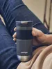 A person holding a Contigo travel mug while wearing jeans and a tan shirt. Náhľad obrázku produktu