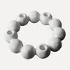 A white beaded ring candle holder on a light gray background. Produktbild-Vorschau