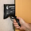 A hand is using a black air pump to inflate a black pneumatic cushion wedged between a wall and a wooden door. Produktbild-Vorschau