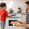 A father and son are in a kitchen, with the son interacting with the oven controls while the father takes out a tray of croissants. Produktbild-Vorschau