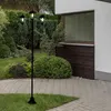 A black metal solar lamp post with three lights stands in a garden next to a house. Produktbild-Vorschau