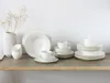 A collection of white porcelain dinnerware, including plates, bowls, and cups, arranged on a wooden shelf against a white wall. Náhľad obrázku produktu