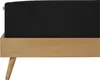 A close-up side view of a black mattress on a light brown wooden bed frame with angled legs. Produktbild-Vorschau